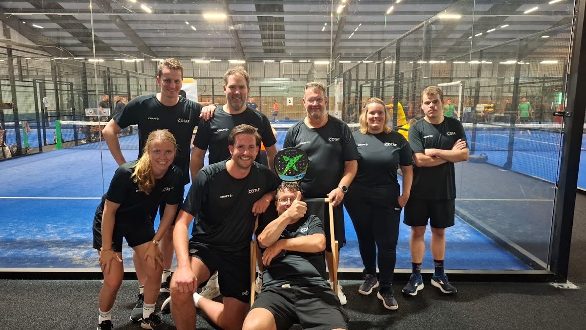 Padelteam in zwarte shirts poseert op blauwe indoorbaan met trofee