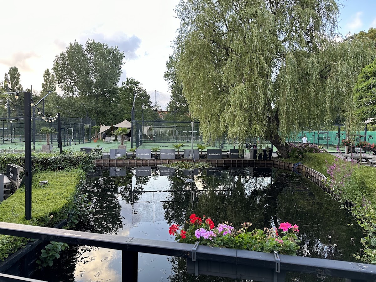 Outdoor padel club met courts aan water, weeping willow, bloemen en tent