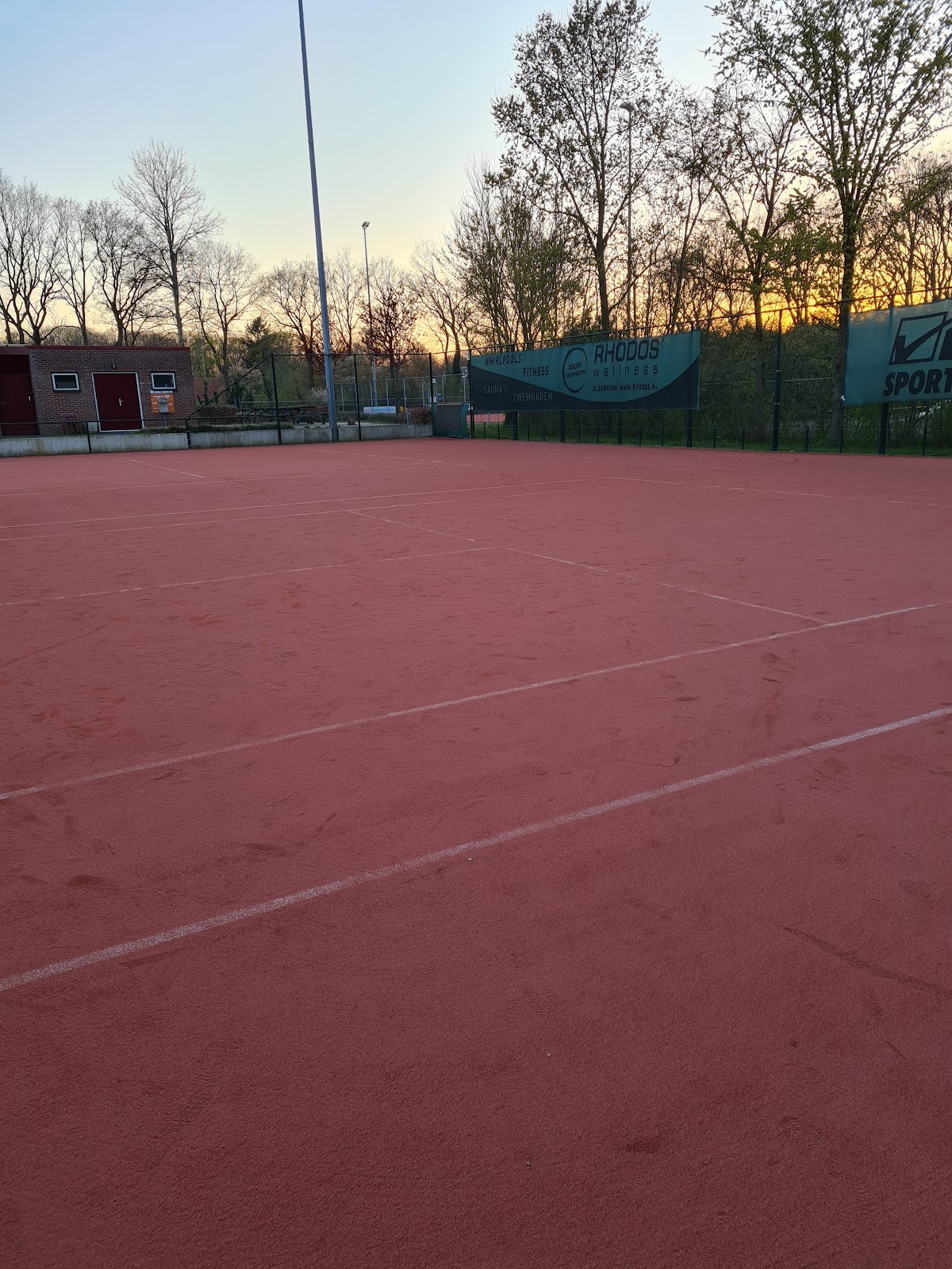 Buitenpadelbaancomplex bij zonsondergang met rode ondergrond en verlichting