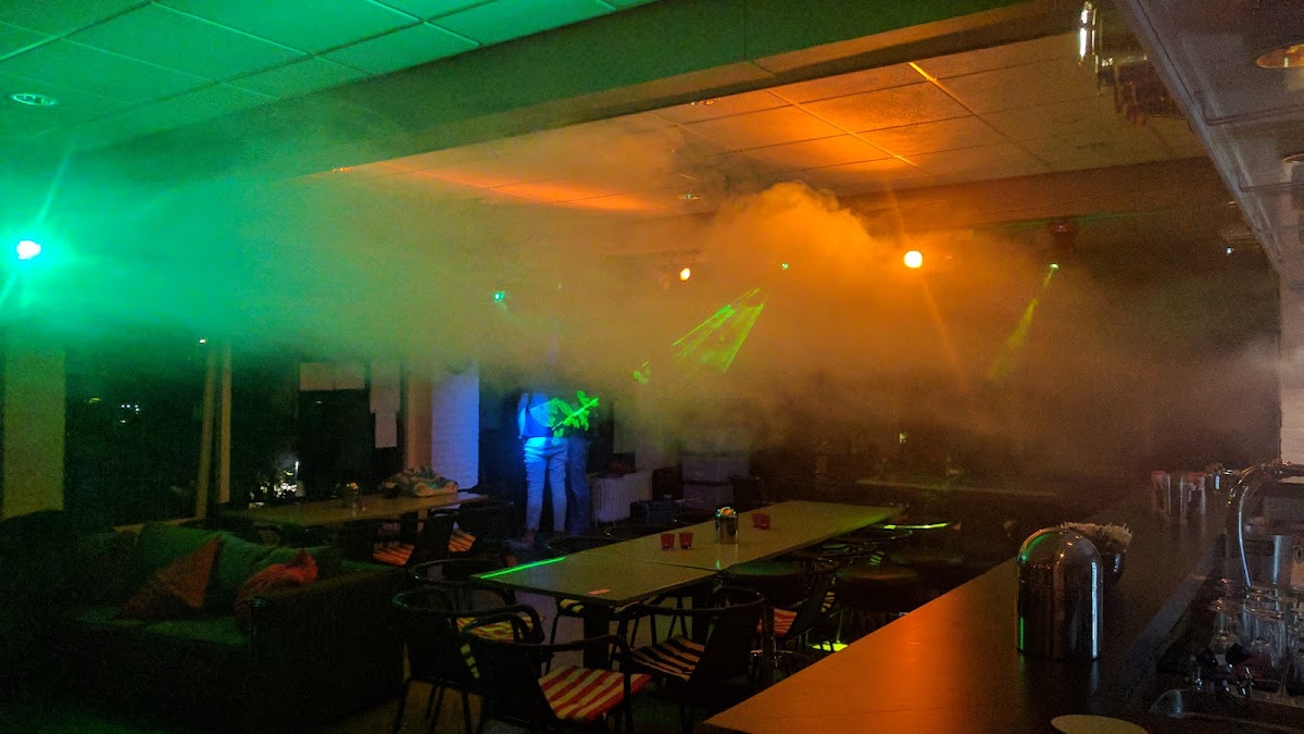 Binnenpadelbaan met bar, groene en oranje verlichting, veel rook/nevel