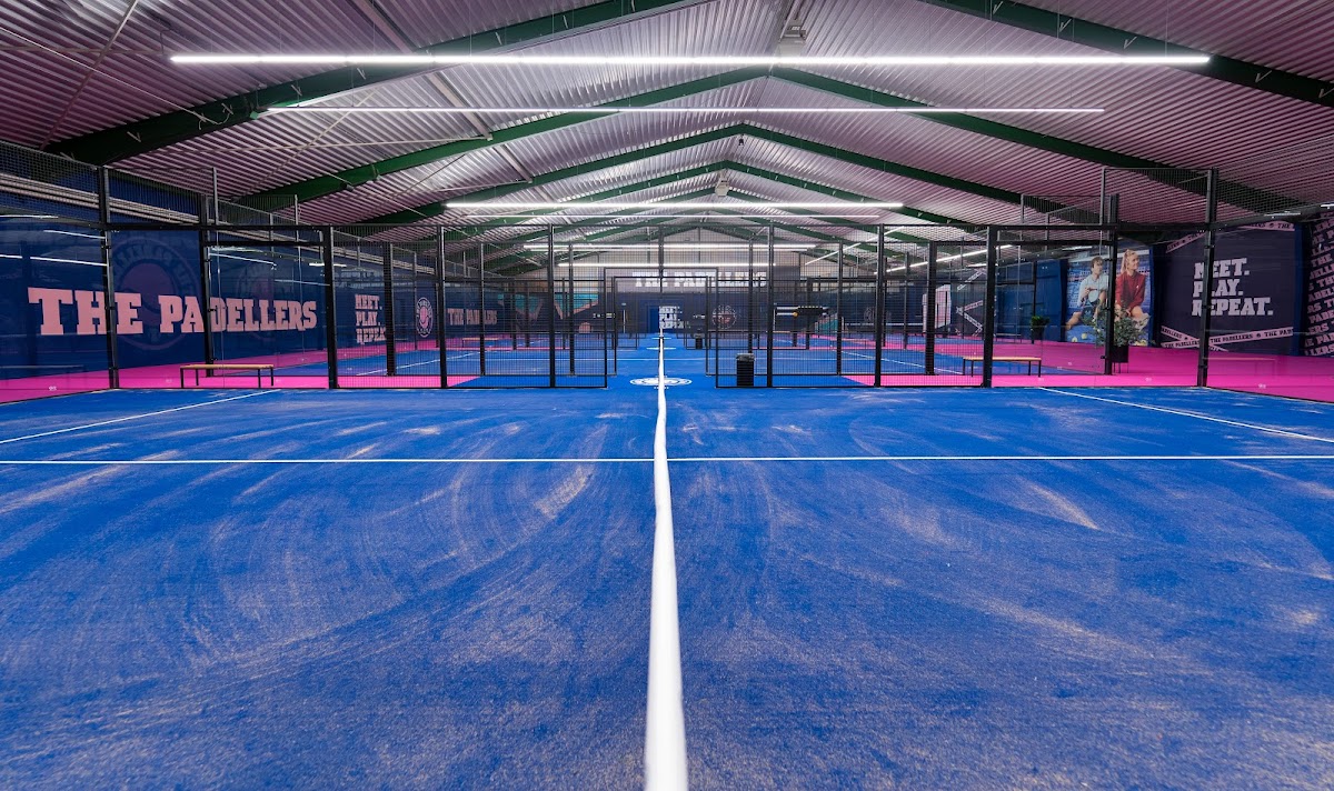 Moderne indoor padelclub met blauwe kunststof banen, roze accenten en LED-verlichting