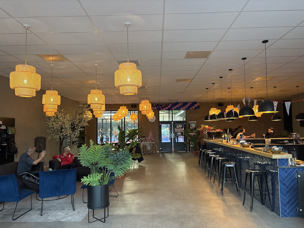 Padel club interieur met bar, hangende lampen en zithoek. Geen padelbaantjes zichtbaar.
