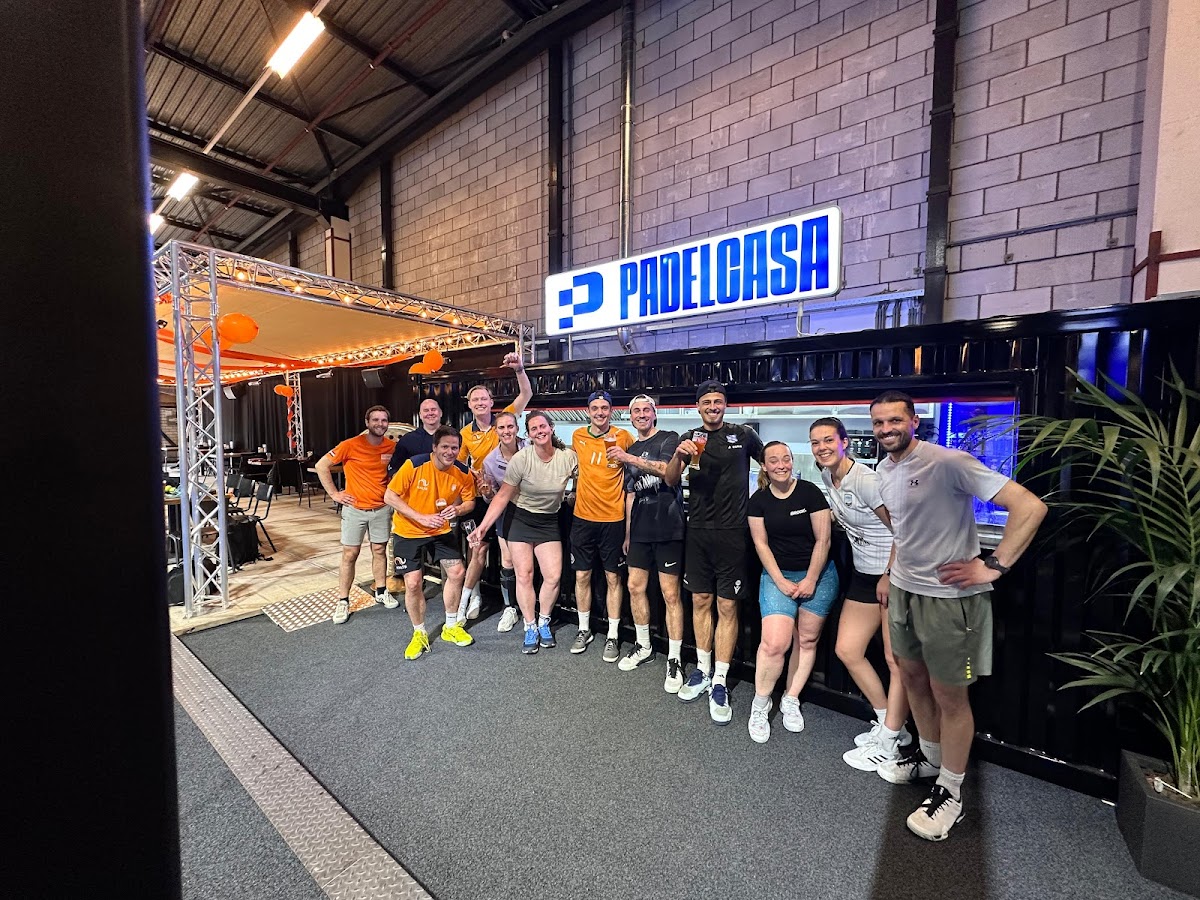 Groep sporters poseert onder PadelCash-banner in moderne indoorpadelbaan