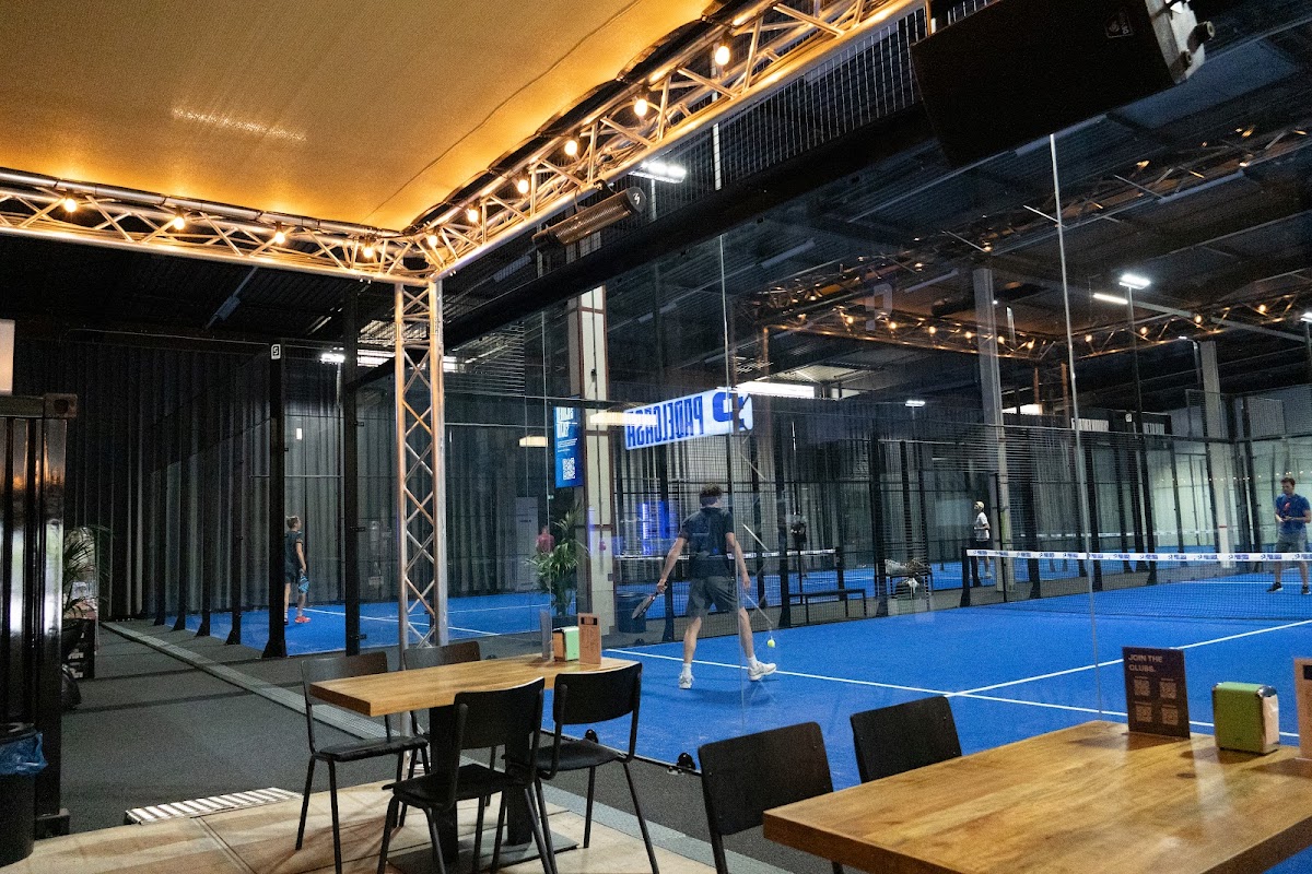 Moderne indoor padelclub met blauwe kunststof courts, verlichting en zithoek