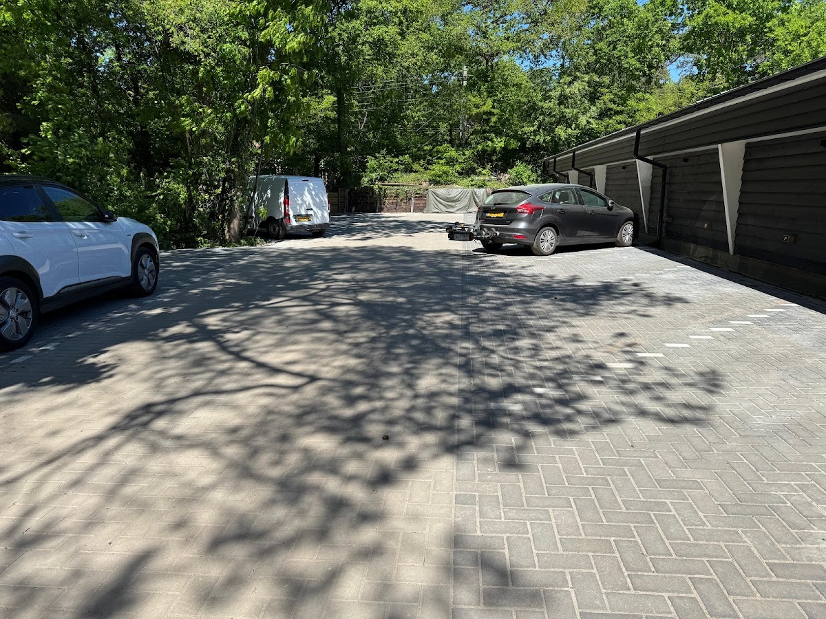 Parkeerplaats met geparkeerde auto's onder loofbomen en carports