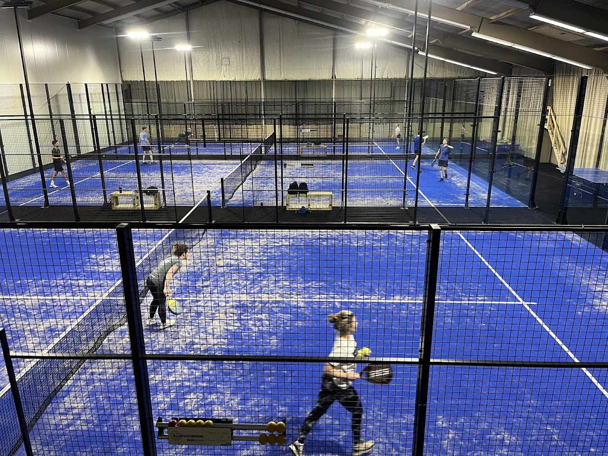 Overdekt padelbaan met blauwe hardcourt, spelers in actie, professionele verlichting