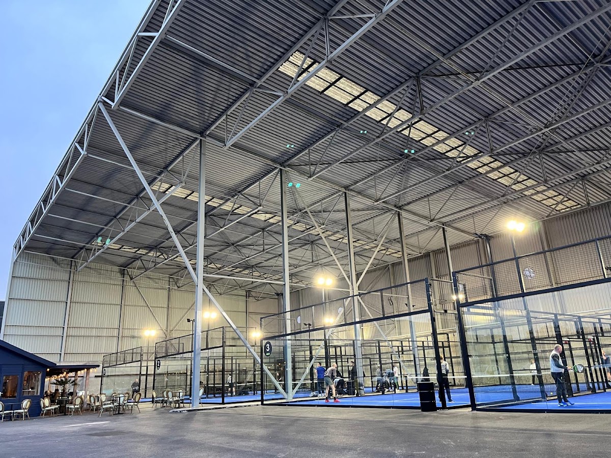 Moderne padelbanen met blauwe ondergrond in grote hal met stalen constructie en verlichting