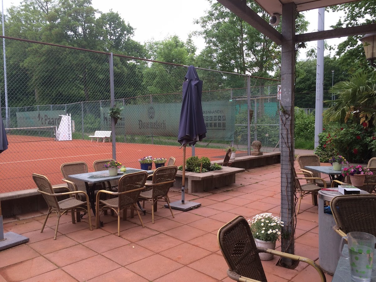 Buitenpadelclub met terras, stoelen en parasol naast tennisbanen