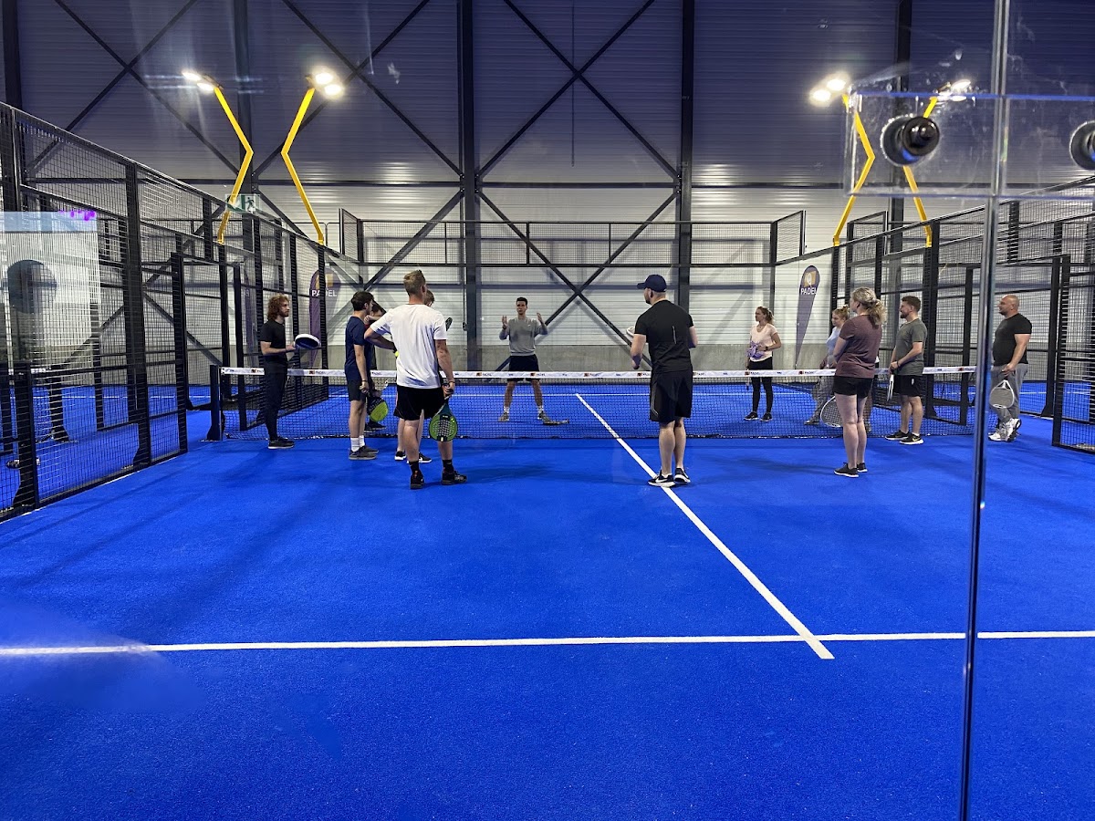 Binnenpadelbaan met blauwe hardcourt, spelers in training onder LED-verlichting