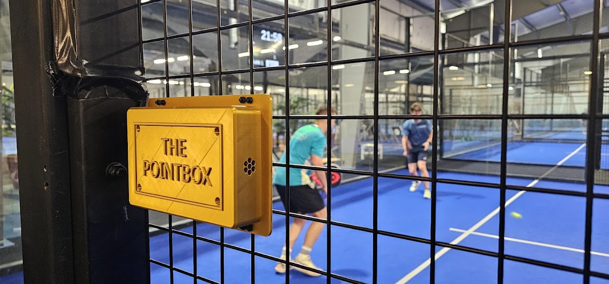 Padelclub met blauwe baan achter glazen wand en gele 'The Pointbox' doos