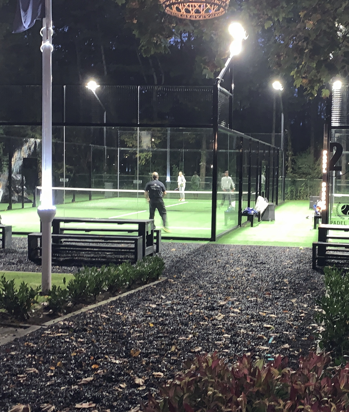Verlichte padelbaan met kunstgras 's avonds, spelers actief op de baan