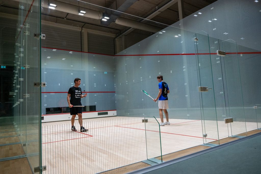 Twee spelers op een indoor padelbaanmet glazen wanden en rode lijnen.