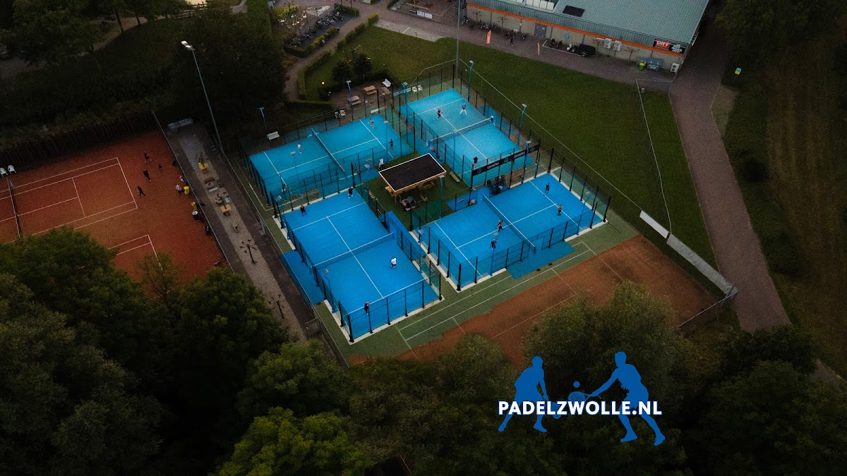 Luchtfoto padelclub met zes blauwe banen, verlichting en faciliteiten omgeven door groen