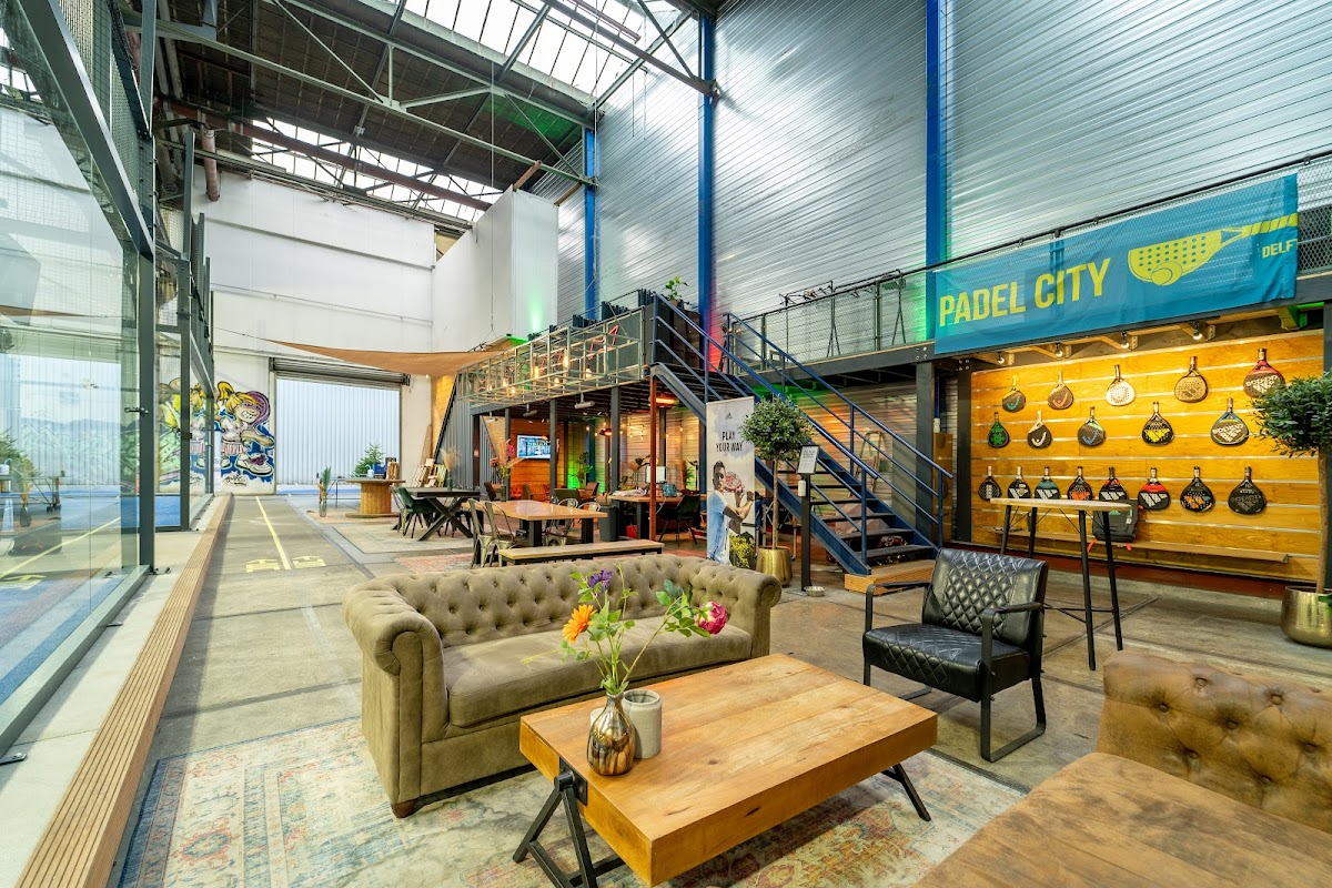Padel City indoor faciliteit met lounge area, gele wand met pannen en trap naar speelvelden