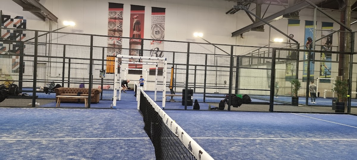 Binnenpadelclub met blauwe QuickPadel-velden, netjes omheind met zwarte framewanden en overhead-verlichting.