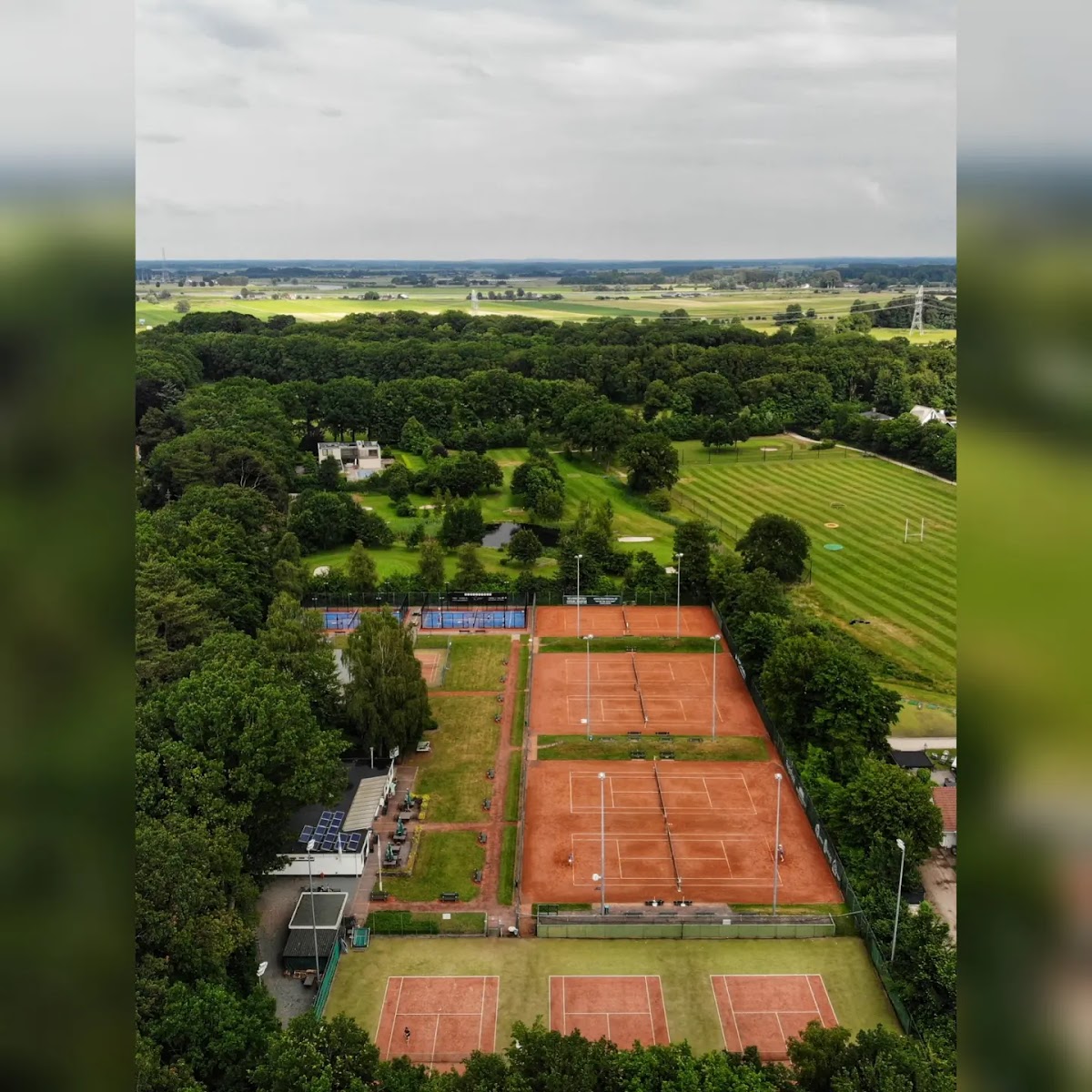 Luchtfoto van padelbanen met rode ondergrond in groene bosrijke omgeving met grasvelden.