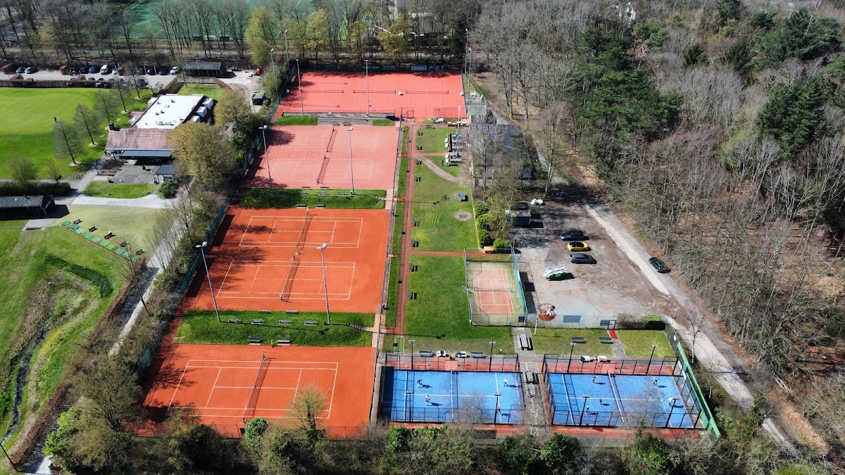 Luchtfoto padel club met oranje en blauwe courts, omgeven door groen grasveld en bomen