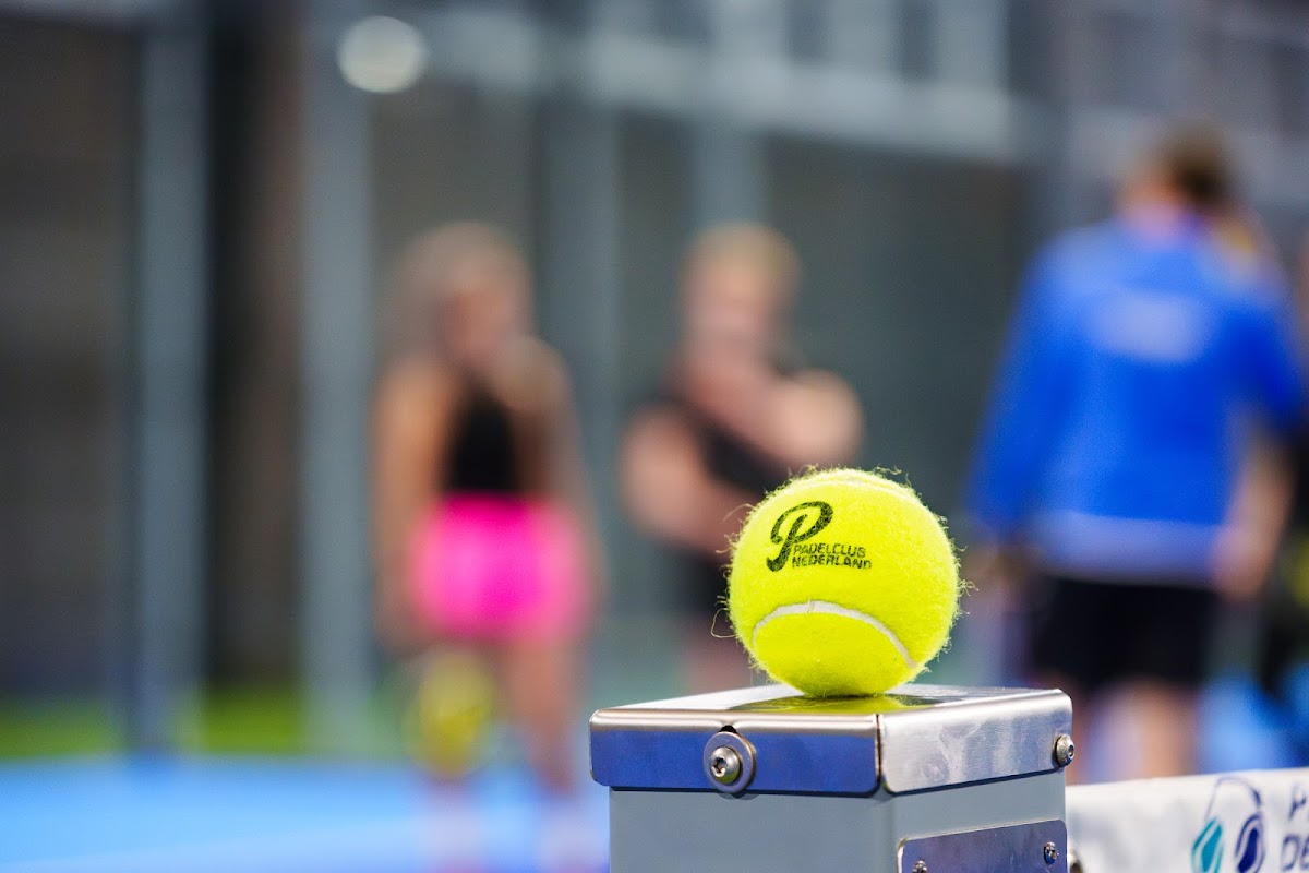 Gele padelbal op tennisnet met spelers op achtergrond op buitenbaan
