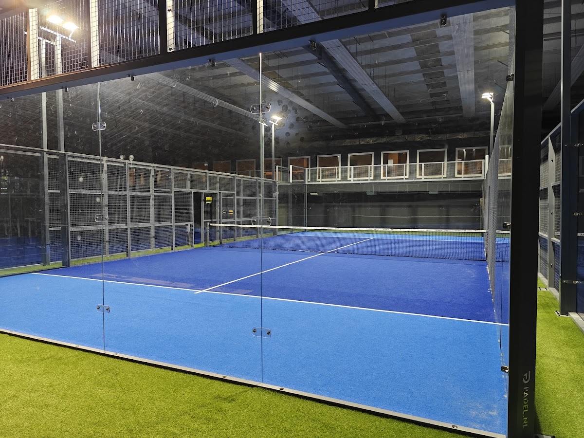 Indoor padelbaan met blauwe hardcourt, verlicht, metalen omheiningen en kunstgras naast de baan