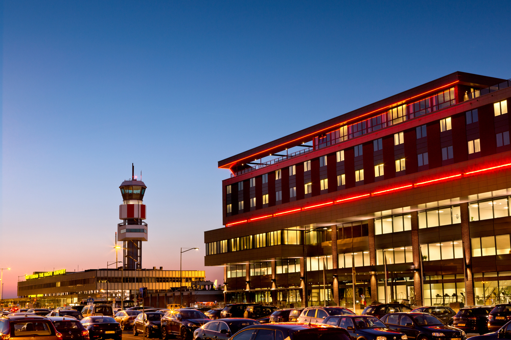 Moderne padelbaan faciliteit met rood verlichte gevel en parkeerplaats bij zonsondergang
