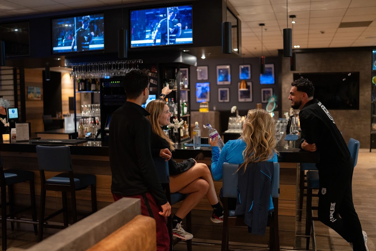 Padel club bar met gasten, tv-schermen en cocktails aan het hoogtetafels
