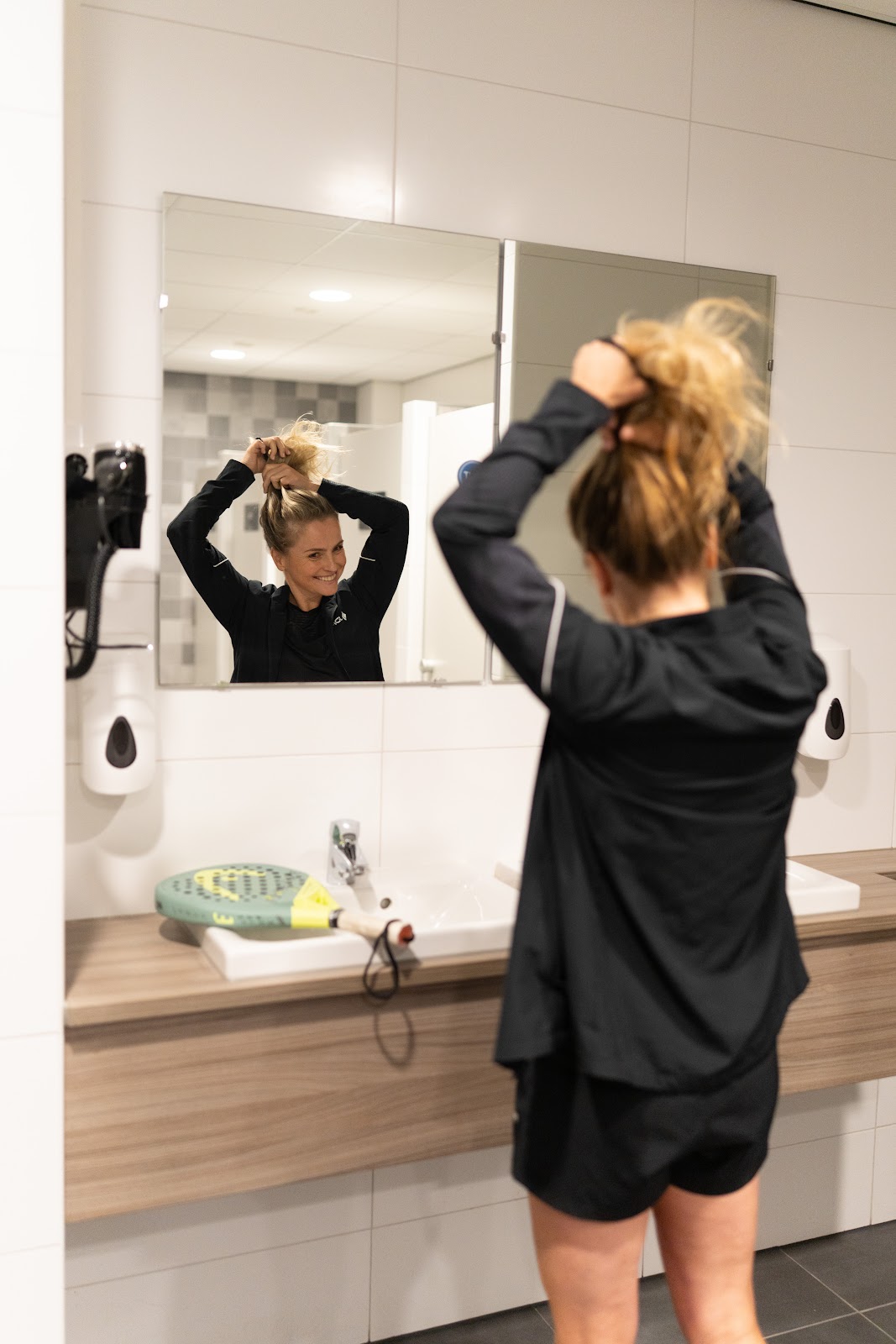 Vrouw in sportkleding bindt haar haren in badkamer met spiegel