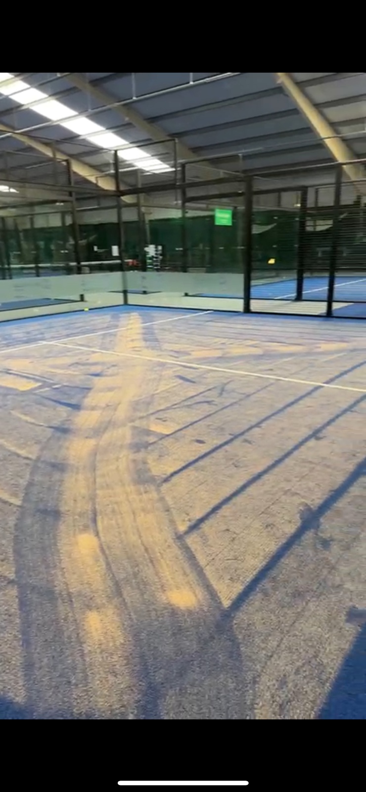 Overdekt padelterrein met blauwe hardcourt, zichtbaar in lage hoek