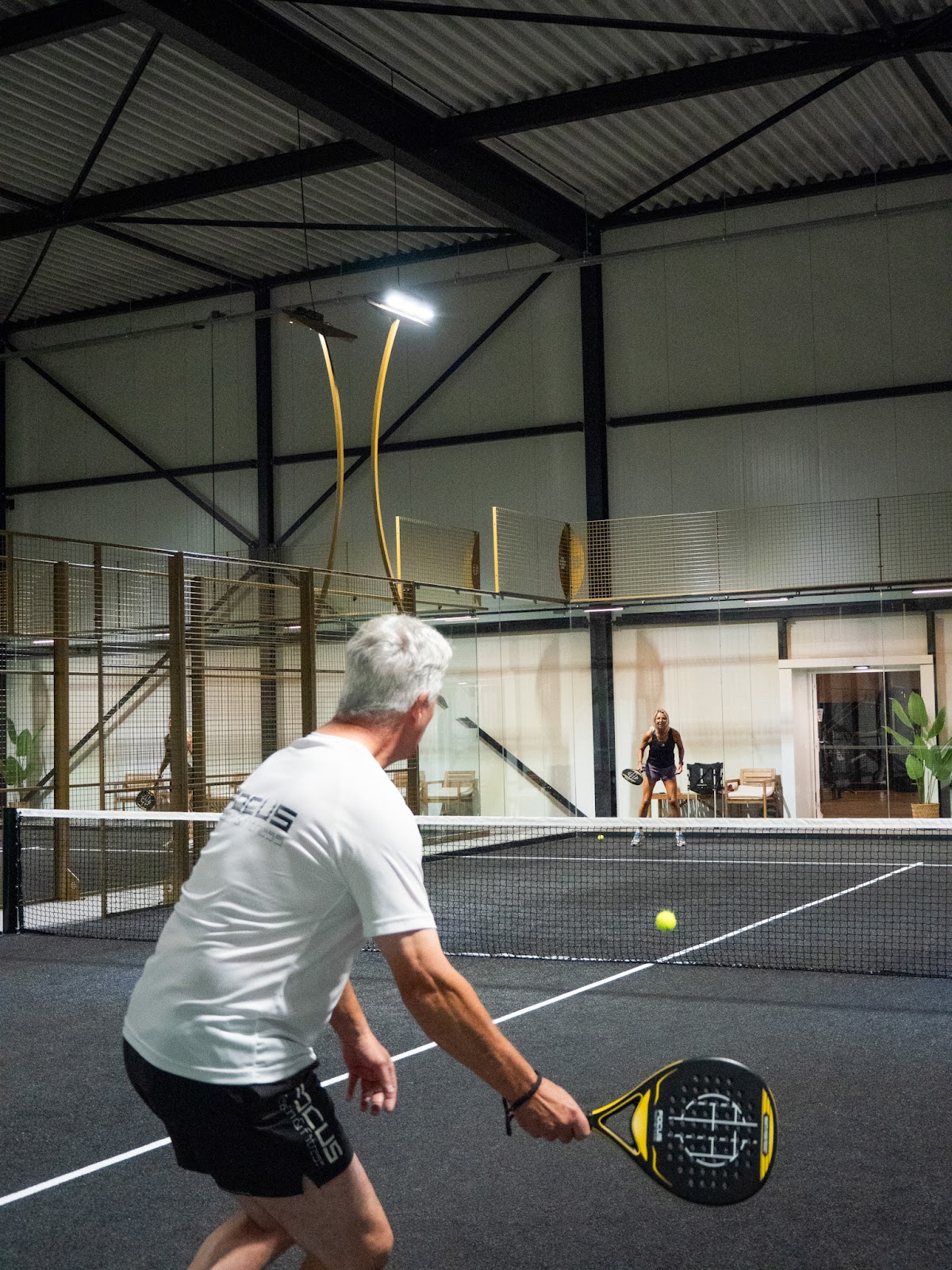 Padel speler in actie op indoor padelbaan met netverlichting