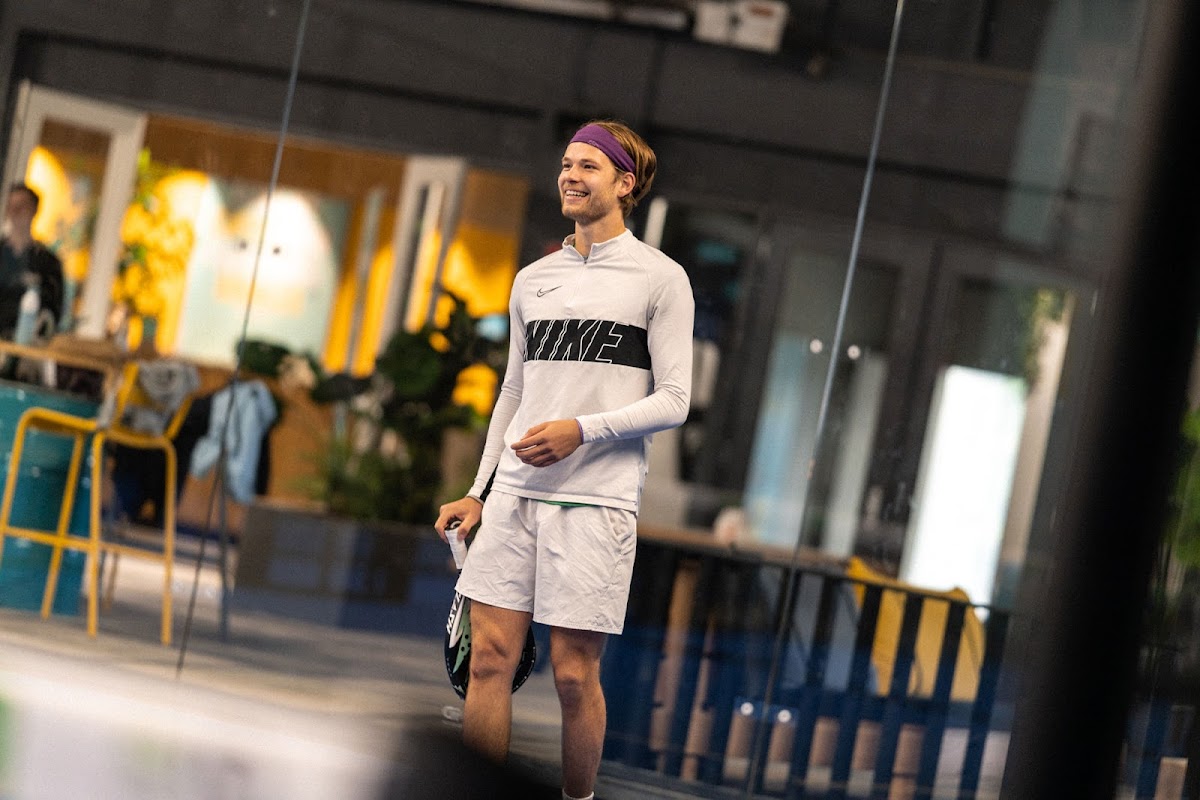 Man jogging in Nike outfit binnen een padel clubfaciliteit met bar op achtergrond
