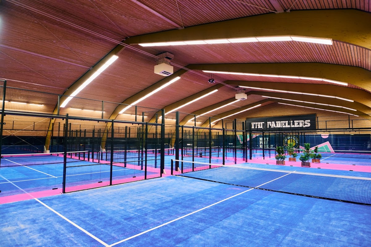 Moderne indoorbaan padelclub met meerdere courts, blauwe en roze velden, zwarte netscheidingen en LED-verlichting.