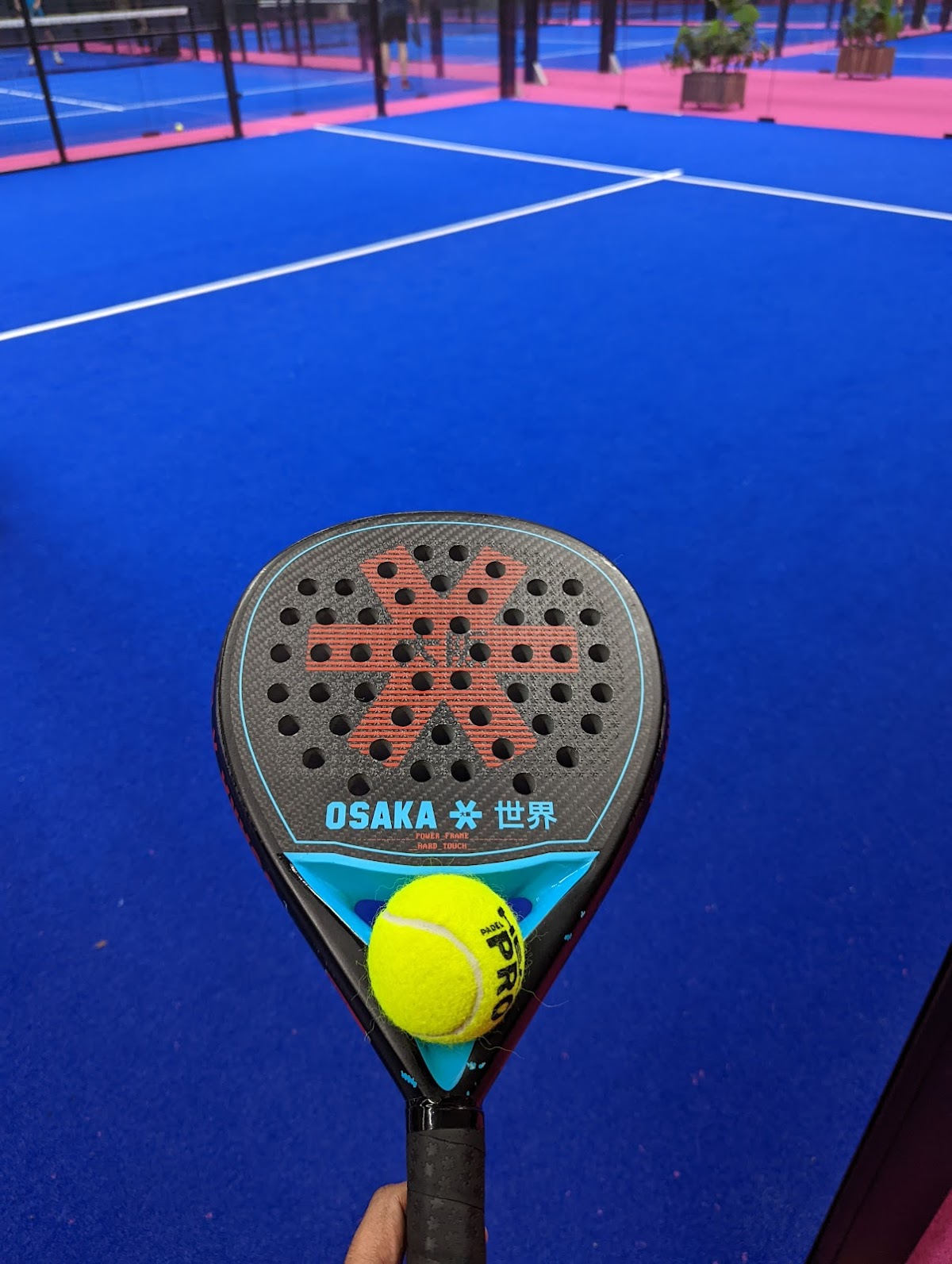 Osaka padelracket met gele bal op blauwe quickpadel baan