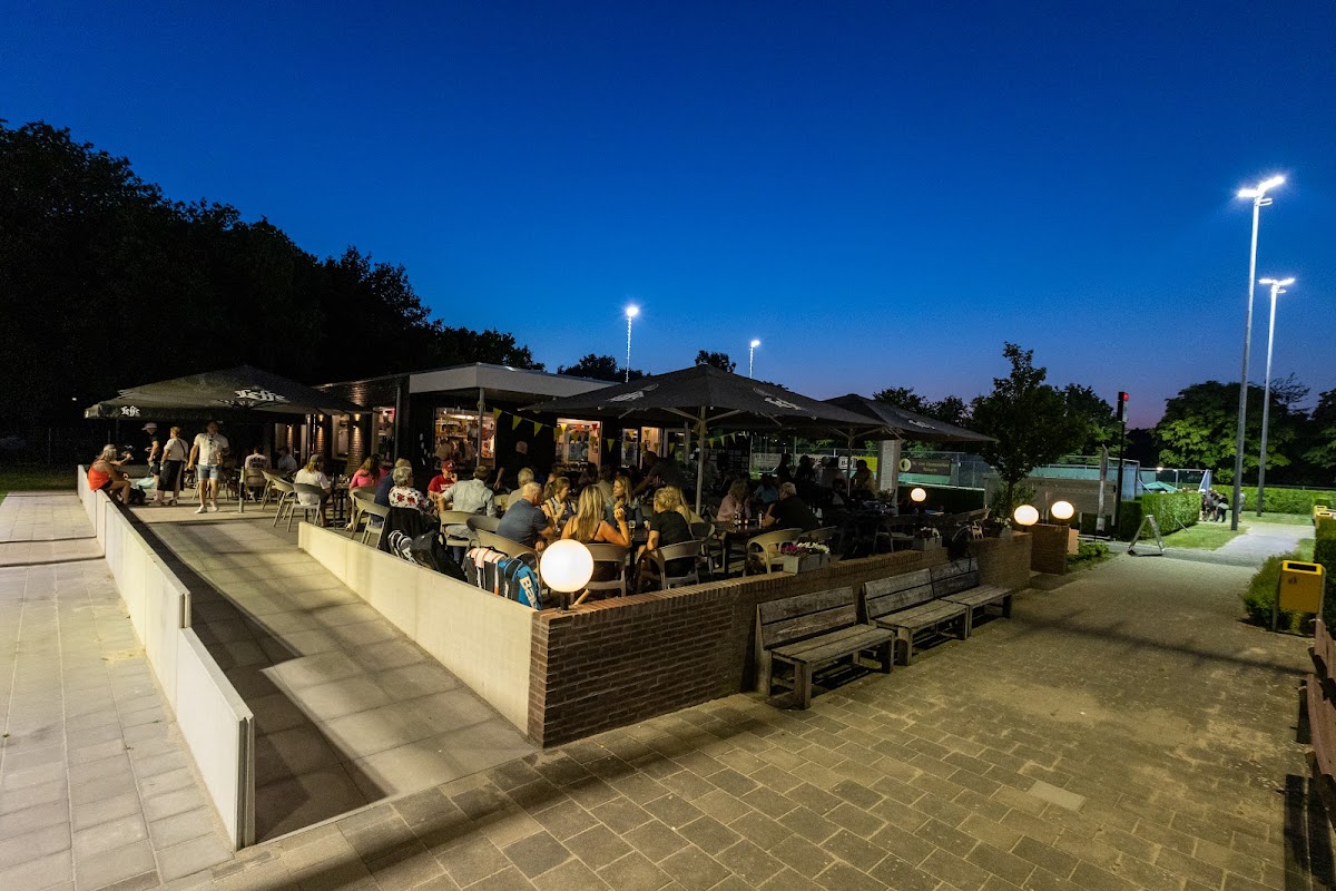 Padel club 's avonds met bezoekers op terras, verlicht door halogeenlampen