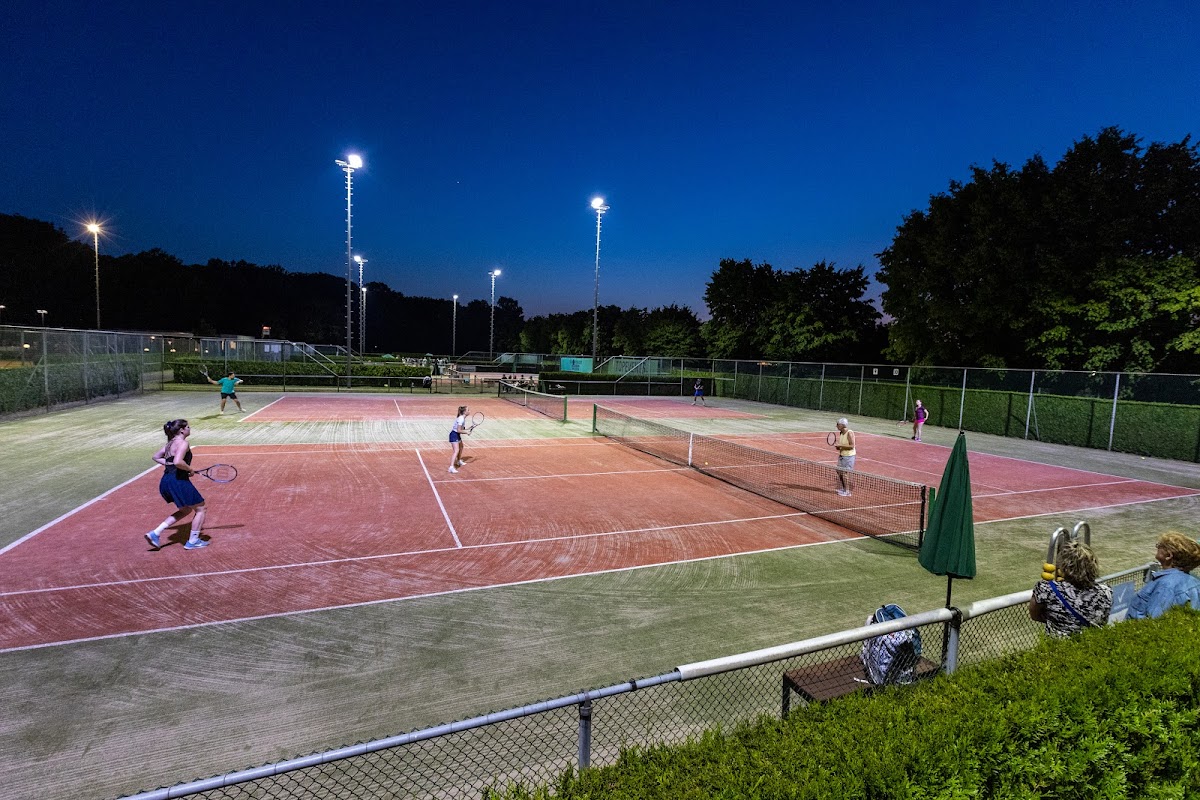 Outdoor padelclub met verlichte banen bij schemering, spelers actief op de velden