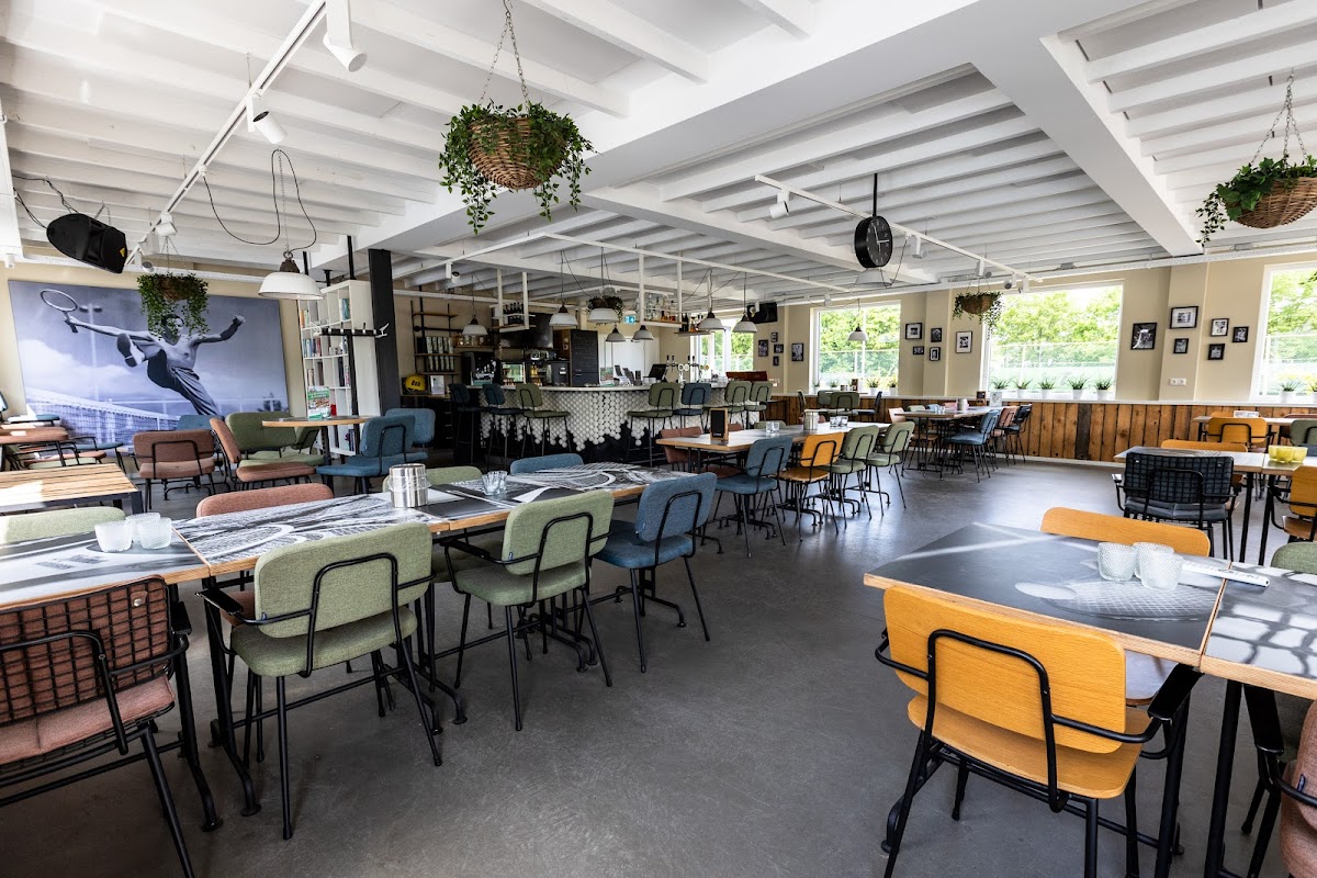 Moderne clubruimte met zithoeken, tafels en bar. Geen padelcourts zichtbaar.