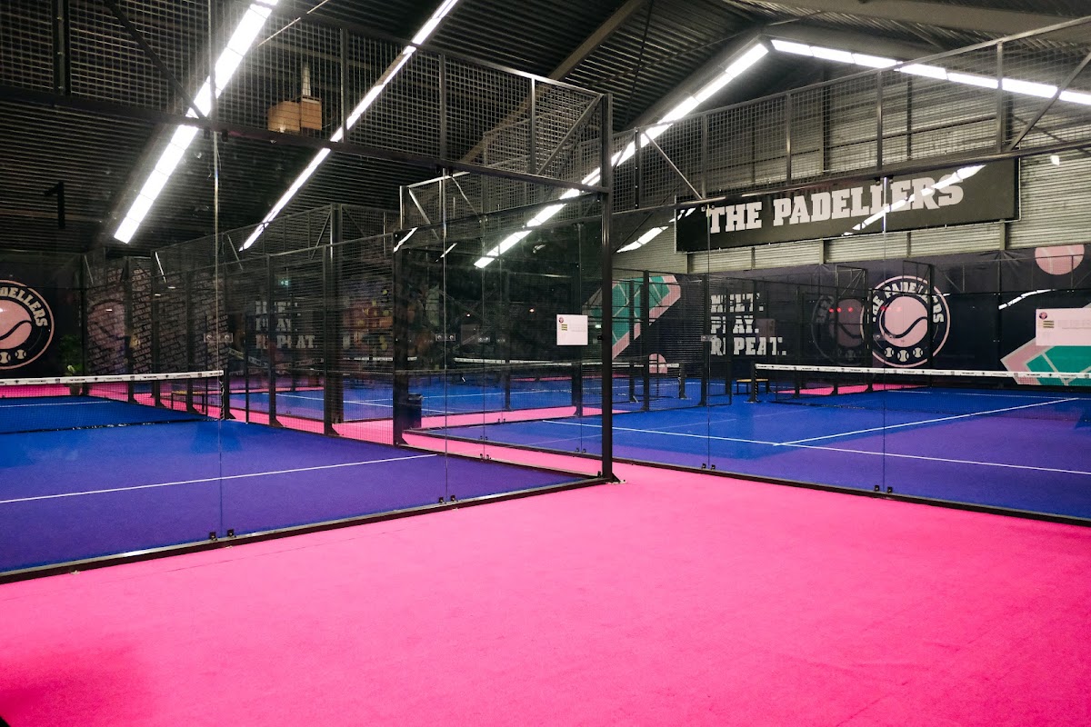 Moderne indoor padelbanen met roze en blauwe vloeren bij The Padeliers