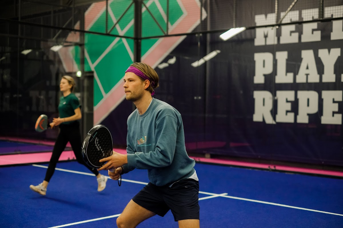 Padelspeler in actie op blauwe binnenbaan met paarse verlichting