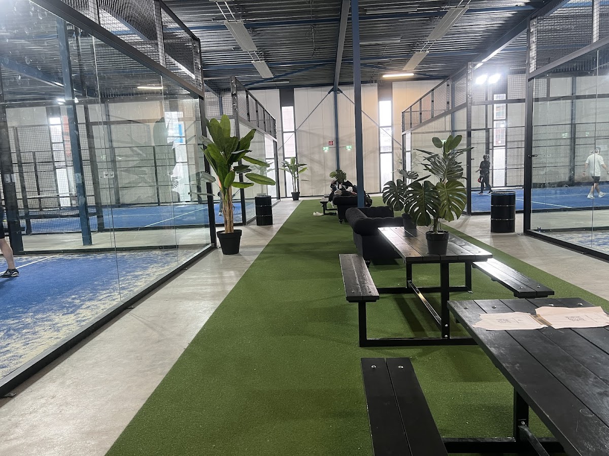 Indoorpadelbaan met groene kunstgras, zithoeken en glazen wanden