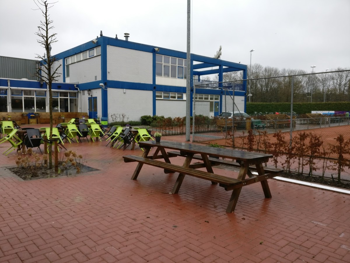 Padelclub met blauw-witte clubhuis, terras met stoelen en houten picknicktafels