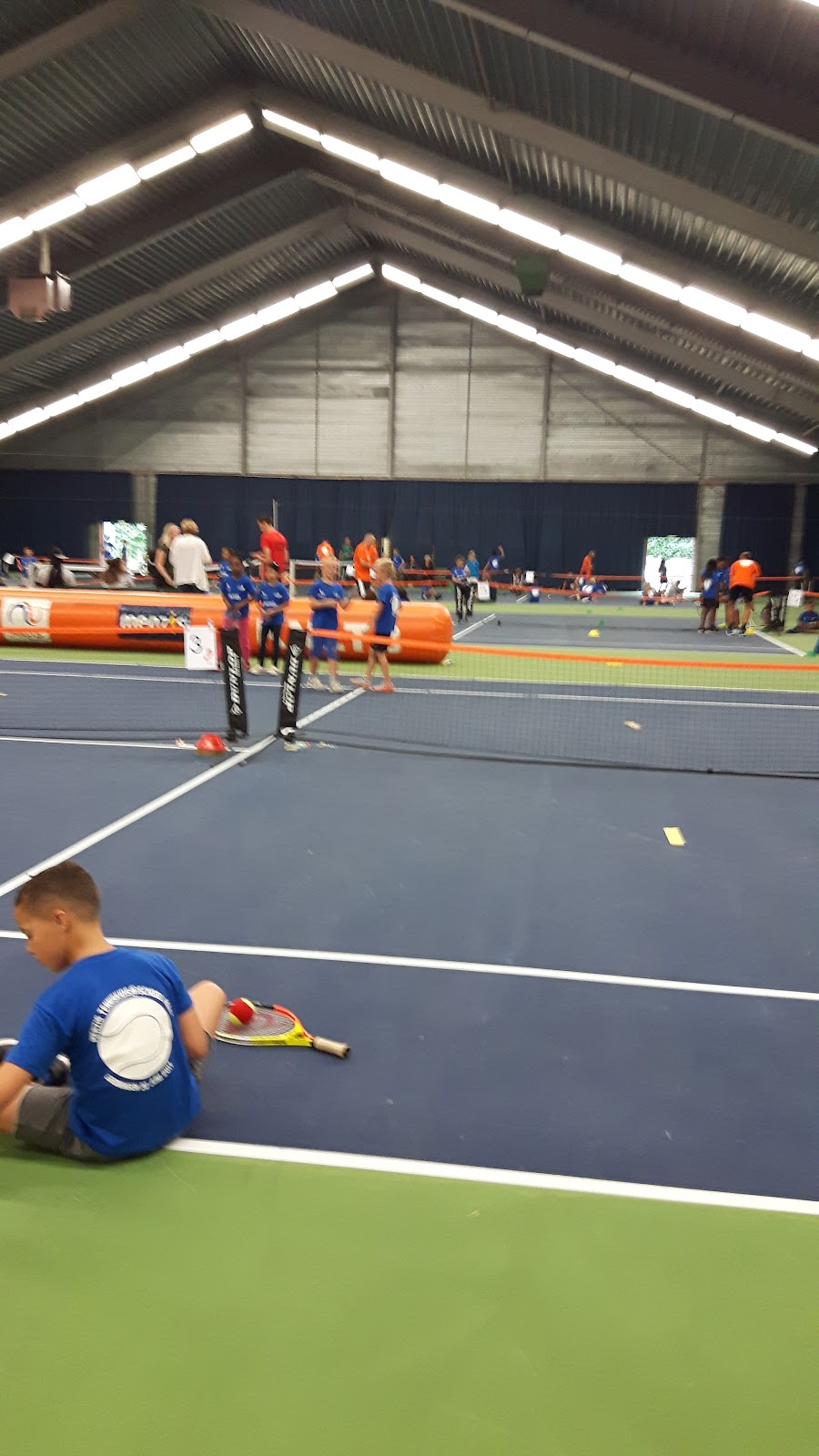 Indoorpadelclub met blauwe hardcourt, kinderen trainen onder LED-verlichting