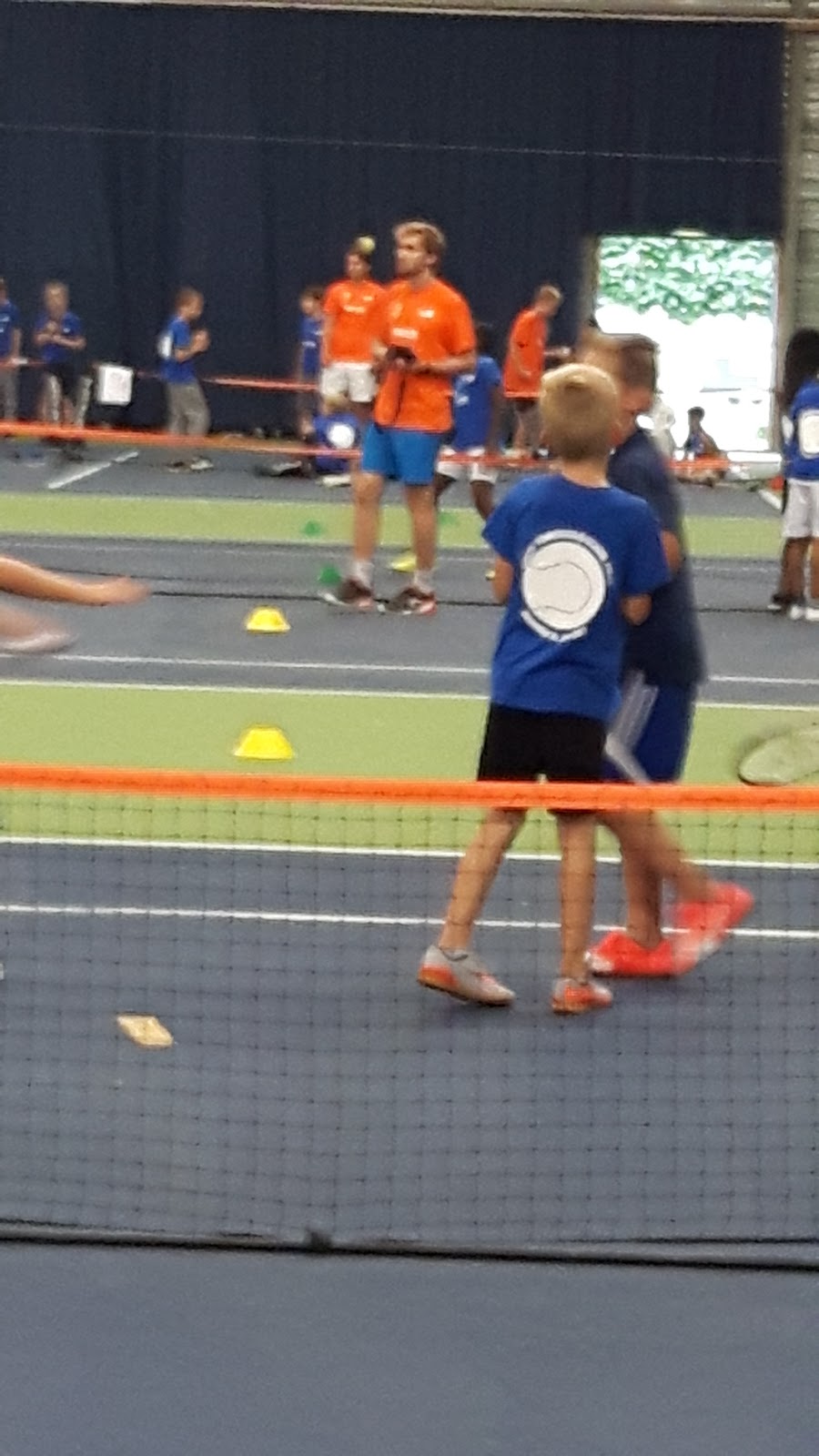 Kinderen trainen op kunstgras padelbaan met oranje en blauwe shirts